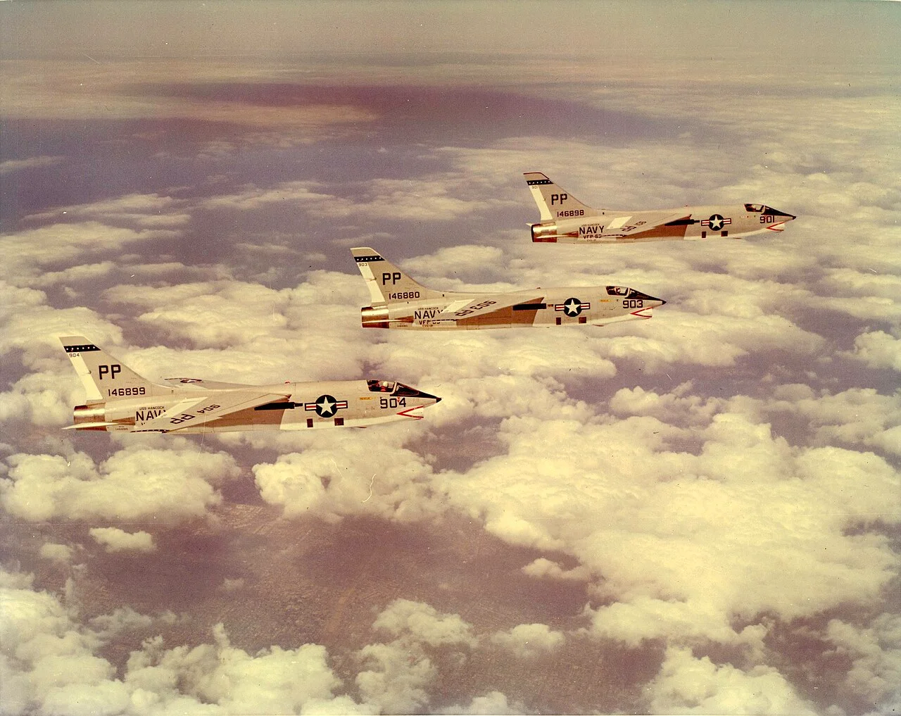 Three photographic-reconnaissance Crusaders flying in formation above clouds.